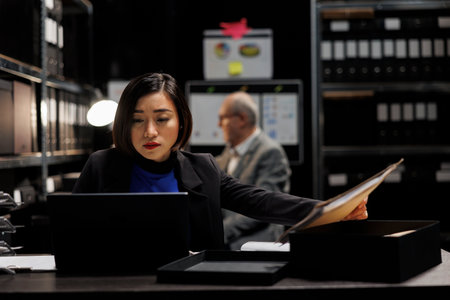 Asian private investigator starting criminal investigation case, comparing criminal investigation details. Detective woman in archive file cabinet office filled with criminology foldersの写真素材