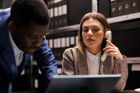 Secretary talking with bookkeeper at landline phone, working together at accountancy report in...