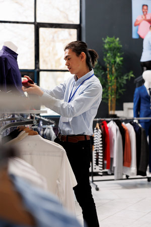 Asian worker arranging formal accessories on store shelf, working at boutique visual in clothing store. Shopping mall employee putting fashionable clothes on hangers. Fashion new collection conceptの写真素材