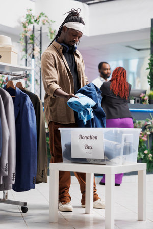 African american man donating old clothes to charity organization in shopping mall. Fashion boutique...