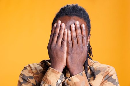 Young adult showing three wise monkeys gesture on camera, covering eyes, mouth and ears as wisdom sayings. African american man advertising silence concept in studio over yellow backgroundの写真素材