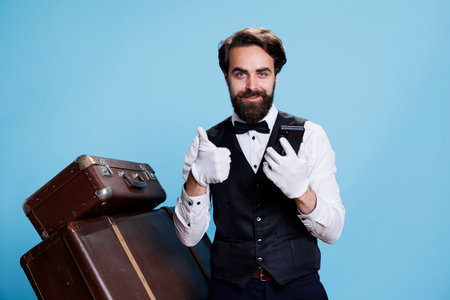Positive bellboy on smartphone app, enjoying excellent news on online website in studio. Confident happy hotel porter in suit and tie finds out great information for tourism industry.の写真素材