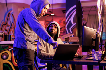 Hackers programming illegal malware on laptop and discussing code on screen. Criminals talking about cyberattack while breaking website on portable computer late at nightの写真素材