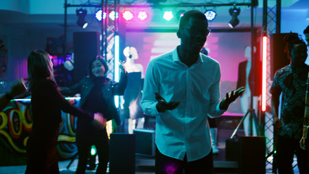Male person partying with friends in discotheque, having fun on electronic music at nightclub. Young...