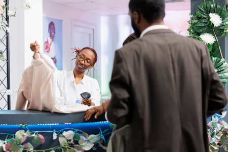Clothing store cashier taking apparel from buyer and scanning barcode at checkout counter. Customers standing in queue while shopping mall employee using pos scanner at cash registerの写真素材