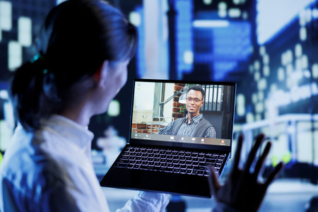 Asian man in videocall with coworker while strolling around city streets at night, giving him work...