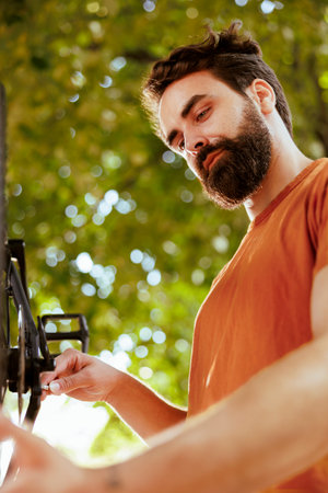 Committed healthy and energetic man adjusting and securing bicycle parts for enjoyable summer cycling. Young male caucasian cyclist repairing bike wheel as yearly maintenance outdoors.の写真素材