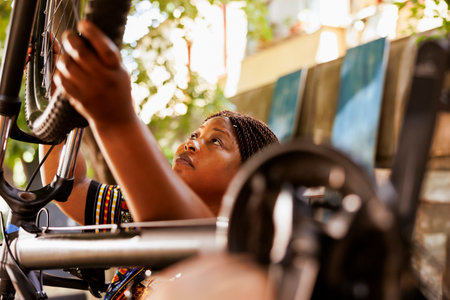 Healthy sportloving black woman securing bike wheel for outdoor leisure cycling. Active young african american female performing annual summer maintenance on bicycle while using tools in yard.の写真素材