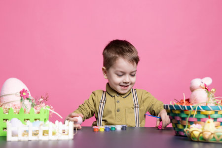 Thrilled young child using watercolors to paint eggs and decorations, creating artistic projects in...