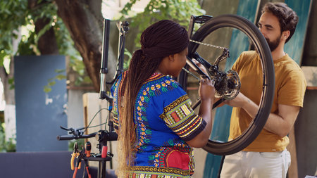 Dedicated multiethnic couple repairing bicycle parts with specialized tools in home yard. Sporty girlfriend and boyfriend using professional equipment for bike components adjustment.の写真素材