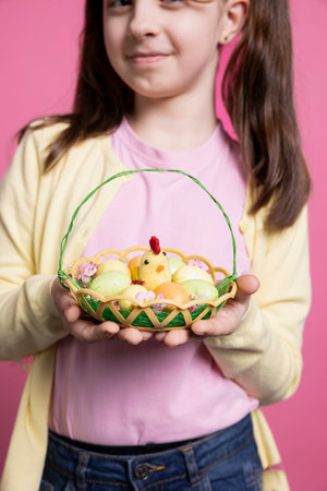 Beautiful small girl with bunny ears holding an egg basket for easter festivity, posing with pretty spring trinkets. Happy and energetic child celebrating the festive season in the studio.の写真素材