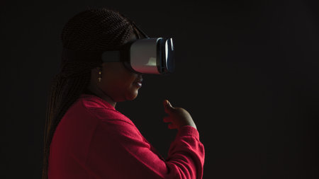 Side-view of creative young female enjoying simulation with interactive technology wearing 3D virtual reality glasses. African american fashionista using a sophisticated VR headset.の写真素材
