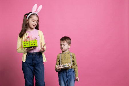 Sweet kids presenting their colorful easter ornaments on camera, little girl showing peace sign and...