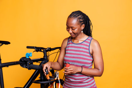 Young african american lady preparing essential tools for mending damaged bicycle. Sporty black woman grabbing several specialized equipment for repairing broken bike against an isolated background.の写真素材