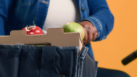Female courier with african american ethnicity delicately moving basket of fresh produce from food...