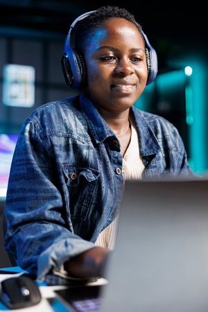 African American freelancer working at home, wearing wireless headphones while browsing the internet...