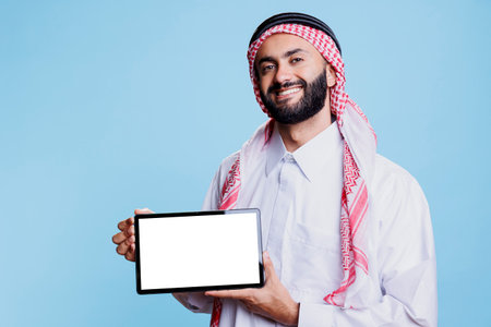 Smiling arab man presenting digital tablet empty screen for app presentation and looking at camera...