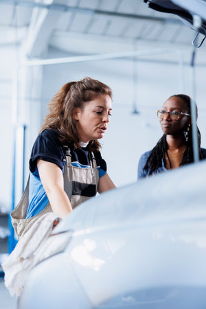 Hardworking mechanic at auto repair shop conducts annual vehicle checkup, informing client about...