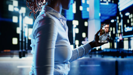 Woman talking with friend in online videocall using smartphone while strolling around empty city boulevards at night. Person showing companion surroundings in urban environmentの写真素材