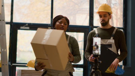 Warehouse employees using smartphone placed on tripod to make video for social media promoting the company. Coworkers filming themselves in storage room showcasing their daily tasksの写真素材