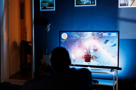 Young adult enjoying time playing shooter games on tv, plugging his console to television in the...