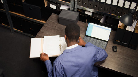 In evidence room, black police officer conducts an investigation using case files and personal...