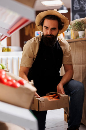 Trader adding crates full of farm grown vegetables from his own garden on zero waste shop shelves. Storekeeper restocking local neighborhood store with chemicals free food itemsの写真素材