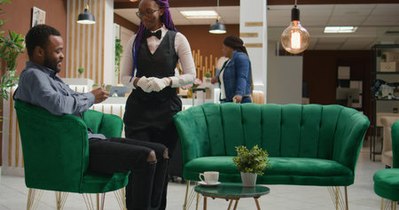 Tourist paying cash for cup of coffee, handing money and tips to woman hotel concierge in lounge...