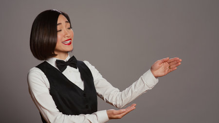 Reception staff doing web advertisement over grey background, pointing at something aside for a marketing commercial. Asian employee working on a promotional ad in studio. Camera B.の写真素材