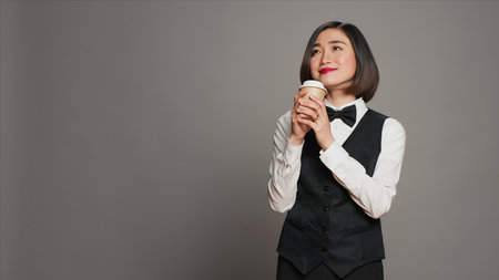 Asian receptionist serving coffee cup in front of camera, taking a break and enjoying hot refreshment. Hotel administrator drinking caffeine beverage, tourism concept. Camera A.の写真素材