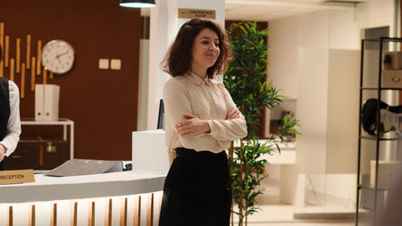 Smiling hotel manager handing folders of tourist accommodation travel booking paperwork to happy receptionist. Cheerful professional staff working in modern resort lobby.の写真素材