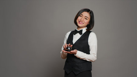 Woman hotel employee ringing front desk service bell in studio, working as a receptionist and...