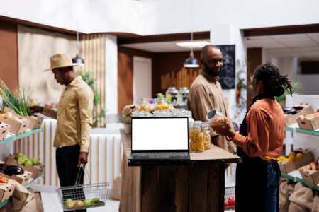 A laptop with an empty white screen display is set down on a wooden counter with customers looking...