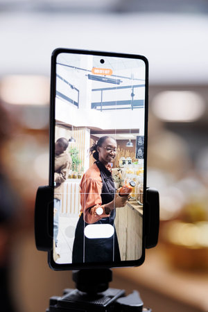 African American store owner uses cell phone and selfie stick for vlogging, promoting sustainable,...