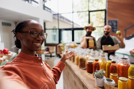 Female customer with a camera, showcasing organic products local store. Black woman creating a vlog with male shopkeepers, emphasizing fresh produce, eco friendly options, and vibrant community.の写真素材