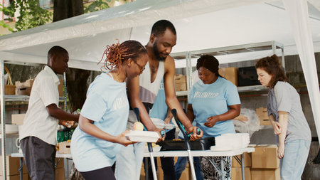 Multicultural non-profit team distributes and delivers humanitarian help to the needy and underprivileged. Black volunteer woman assists african american guy with crutches at food drive. Handheld.の写真素材