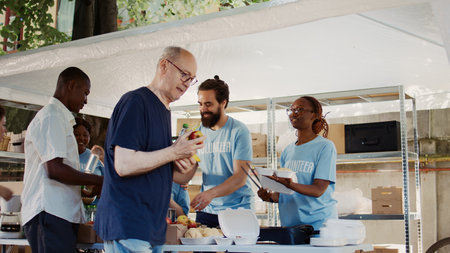 In this shot we see the poor and homeless people receiving free food and nourishments from the hunger relief team of volunteers. Charity workers donating fruits and meals to the underprivileged.の写真素材