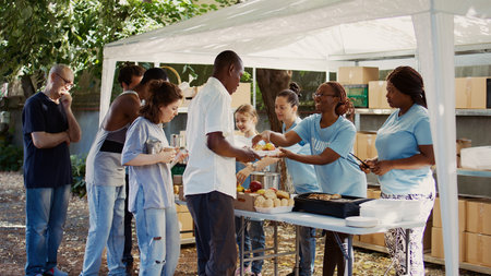 People from many backgrounds assemble outside to distribute non-perishable donations and help the poor and homeless. Multiracial volunteers provide needy individuals with free, freshly prepared meals.の写真素材