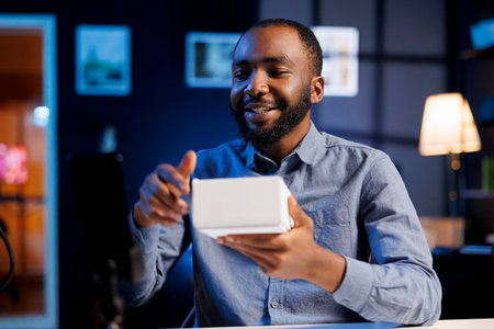 African american online show host being sponsored by partnering brand to do unboxing video on streaming platform. BIPOC man does influencer marketing, presenting viewers product advertisementの写真素材