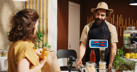 Happy woman in zero waste supermarket using paper bag to carry pantry staples to checkout counter. Green living customer in local neighborhood grocery shop doing shopping for cooking ingredientsの写真素材