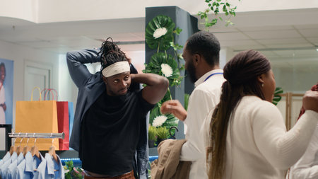 Man helping friend find stylish formal clothes on hangers in fancy fashion boutique. Shopper trying on latest exquisite designer clothing men shirts collection in premium showroomの写真素材