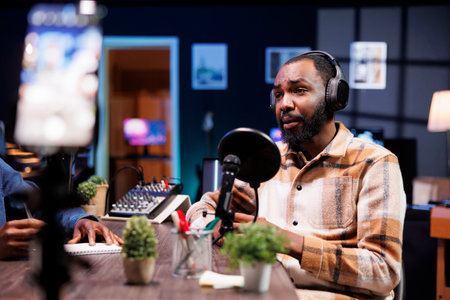 African American influencer in the studio, using a high-tech microphone for an internet program on a livestreaming channel. Man doing a podcasting session with quality streaming recording equipment.の写真素材