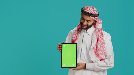Arab guy presents greenscreen display over studio background, showcasing blank copyspace mockup...