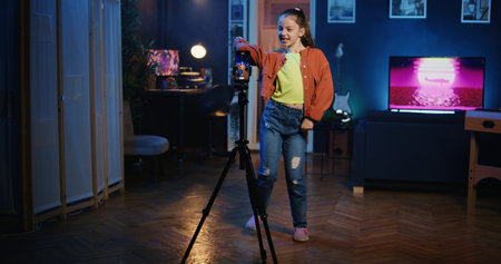 Dolly in shot of kid media star recording trendy dance video clip for social media using cellphone on tripod stabilizer, entertaining audiences. Gen z influencer recording content using smartphoneの写真素材