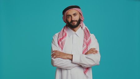 Man in religious thobe and kufiyah, being pleased indicating muslim cultural identity and national tradition. Middle eastern person dressed in robe and checkered headscarf.の写真素材