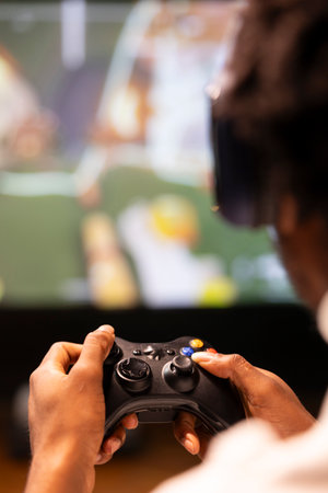 Close up shot of controller held by gamer sitting in front of gigantic television set displaying...