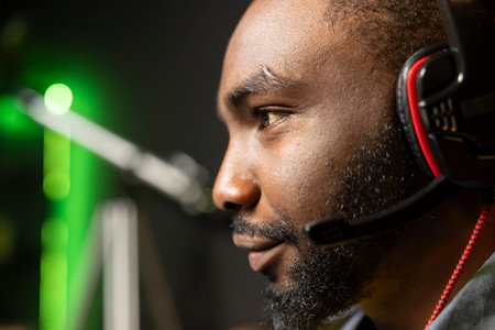 Smiling BIPOC man has fun playing videogames on PC while chatting with teammates through headphones...