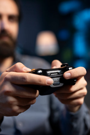 Close up shot of controller held by gamer at home gaming and enjoying leisure time. Focus on gamepad used by man in blurry background in neon lit living room playing videogame on console, relaxingの写真素材
