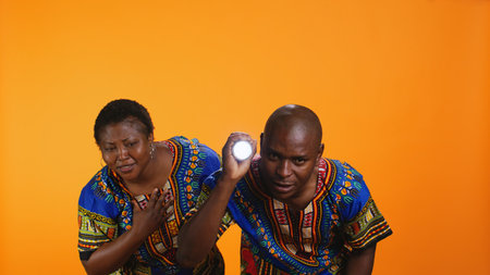Afraid woman hiding behind her husband to investigate something, young brave man using flashlight to see where the scary noises come from. Scared anxious people searching for thing in studio.の写真素材