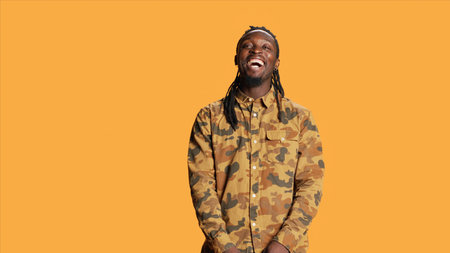 Joyful person enjoying studio shoot and laughing, making jokes on camera and acting playful. Silly funny african american man having fun over orange background, relaxed cool guy.の写真素材